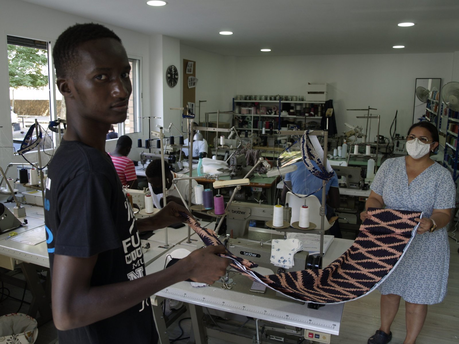 Personas participantes trabajan con maquinaria textil industrial en un taller de formación sociolaboral, elaborando piezas de tela.