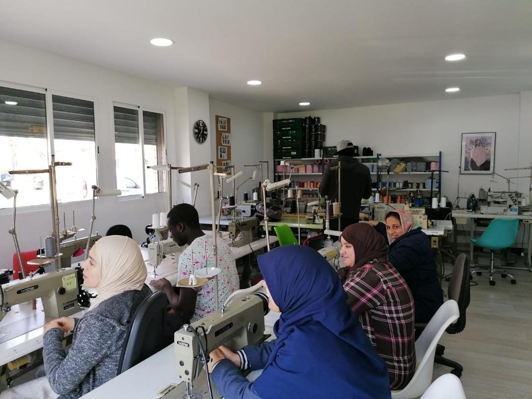 Personas cosiendo en el Taller Textil Solidario del Centre Sant Martí, trabajando con máquinas industriales en un espacio formativo.